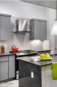 kitchen featuring wall chimney range hood, gray cabinetry, stainless steel range, and tasteful backsplash