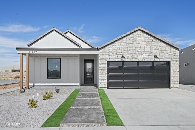 view of front of house with a tile roof, stone siding, board and batten siding, concrete driveway, and a garage