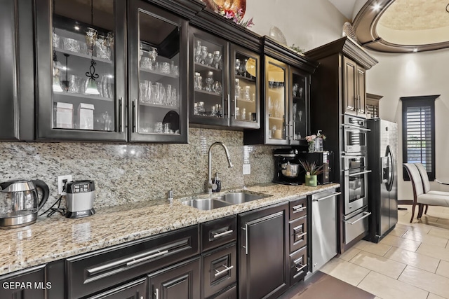 kitchen with backsplash, light tile patterned floors, stainless steel appliances, sink, and light stone countertops