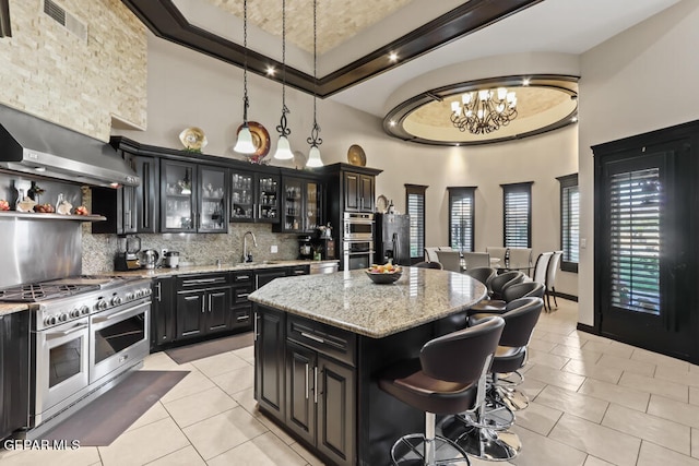 kitchen with a kitchen island, a notable chandelier, stainless steel appliances, light stone counters, and a towering ceiling