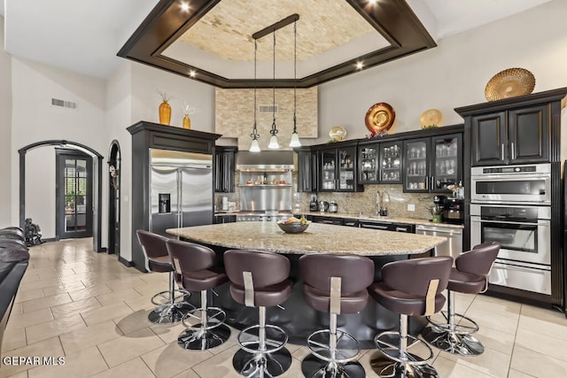 kitchen featuring backsplash, a kitchen bar, a center island, stainless steel appliances, and light stone counters