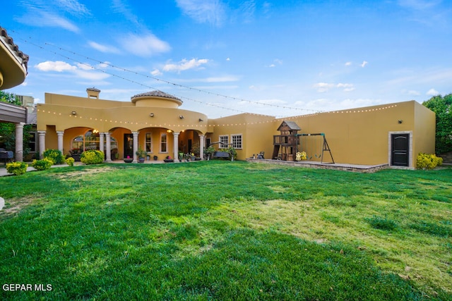 back of house featuring a playground and a lawn