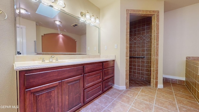 bathroom featuring tile patterned floors, vanity, a tile shower, and a skylight