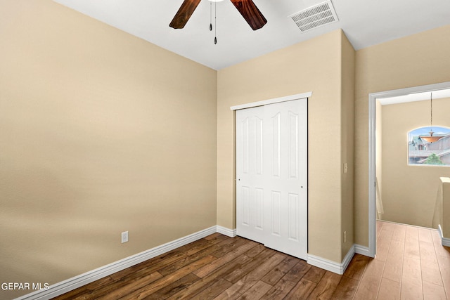 unfurnished bedroom featuring wood finished floors, visible vents, baseboards, ceiling fan, and a closet