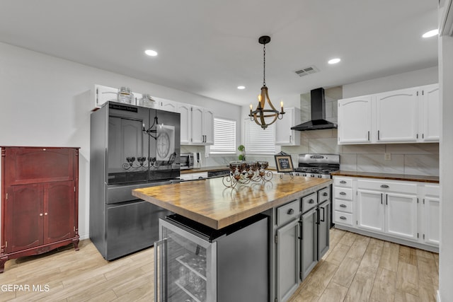 kitchen with beverage cooler, appliances with stainless steel finishes, wall chimney exhaust hood, and white cabinets