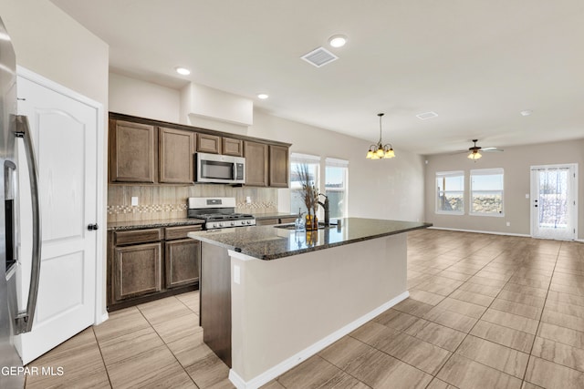 kitchen with dark stone counters, a healthy amount of sunlight, ceiling fan with notable chandelier, and appliances with stainless steel finishes