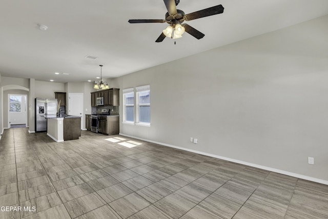 unfurnished living room with a sink, ceiling fan with notable chandelier, baseboards, and arched walkways