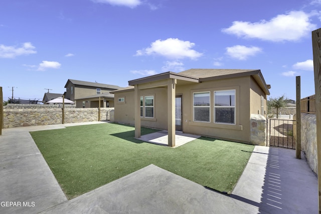 back of house with fence, stucco siding, a yard, a patio, and a gate