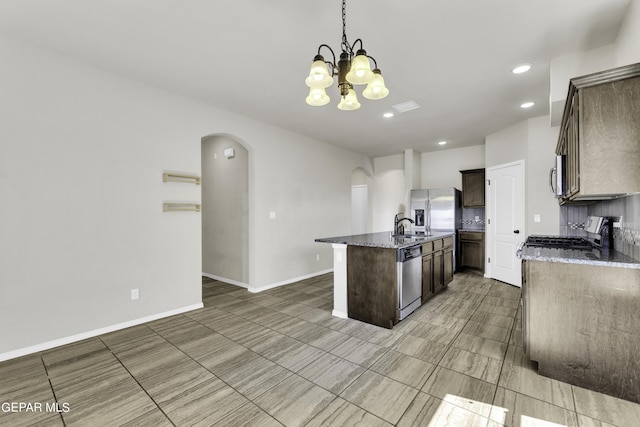 kitchen with a kitchen island with sink, dark stone countertops, stainless steel appliances, arched walkways, and a chandelier