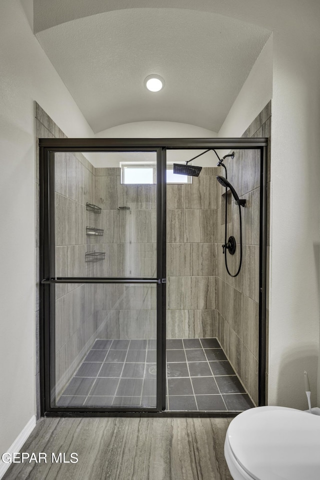 bathroom with a shower stall, toilet, wood finished floors, and lofted ceiling