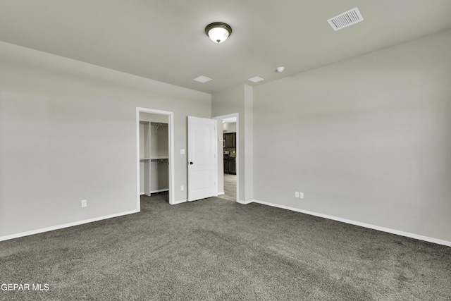 unfurnished bedroom with baseboards, visible vents, a closet, a walk in closet, and dark colored carpet