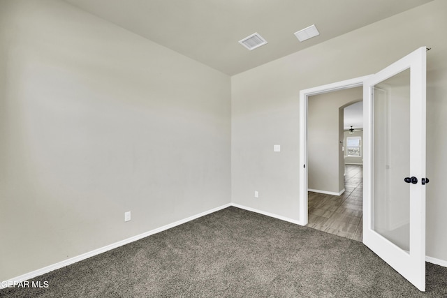 carpeted spare room featuring arched walkways, visible vents, and baseboards