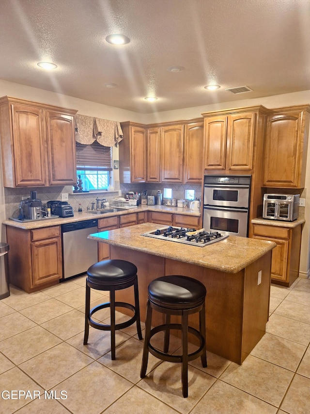 kitchen with a kitchen island, a kitchen bar, light tile patterned floors, appliances with stainless steel finishes, and a textured ceiling