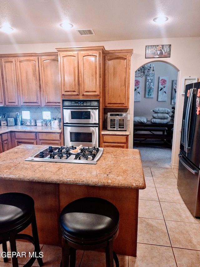 kitchen with light stone counters, appliances with stainless steel finishes, light tile patterned floors, and a kitchen breakfast bar