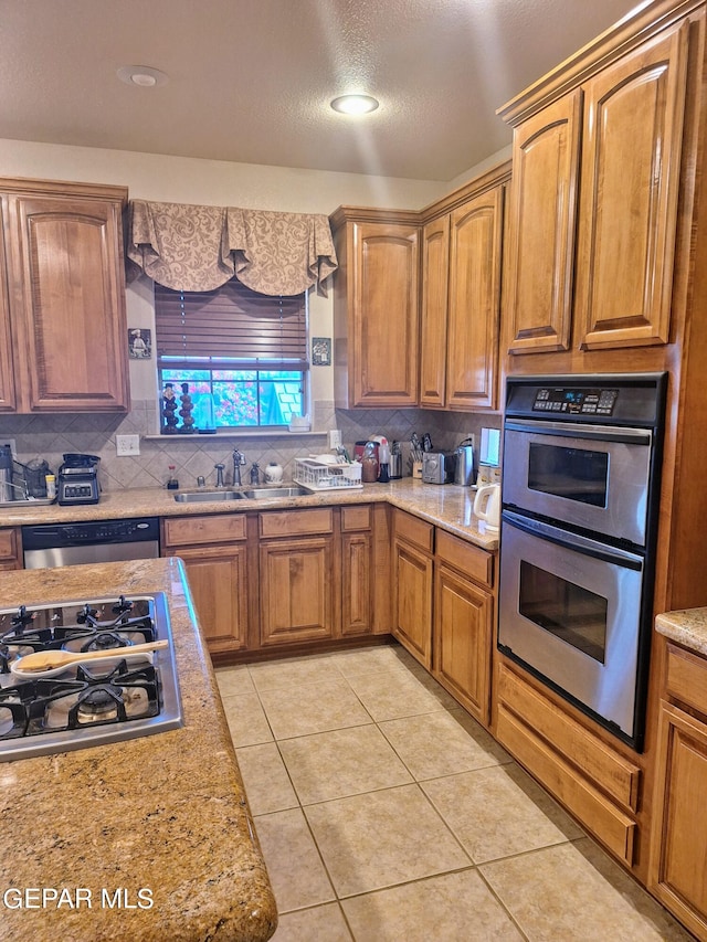 kitchen featuring decorative backsplash, light stone counters, light tile patterned flooring, stainless steel appliances, and sink