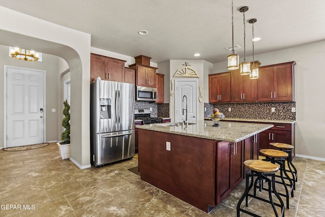 kitchen featuring decorative backsplash, appliances with stainless steel finishes, a kitchen island with sink, light stone countertops, and sink