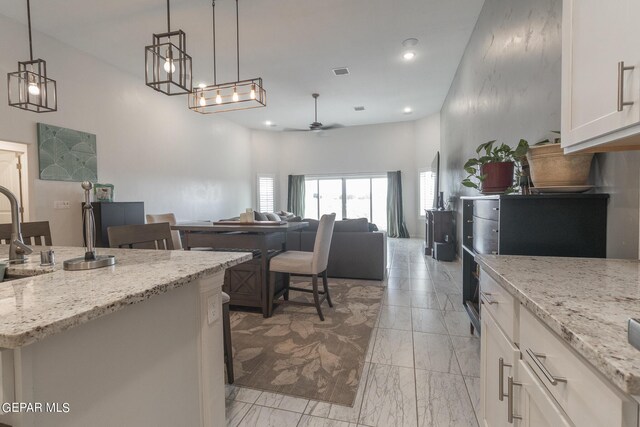 kitchen featuring light stone counters, ceiling fan, white cabinets, and hanging light fixtures