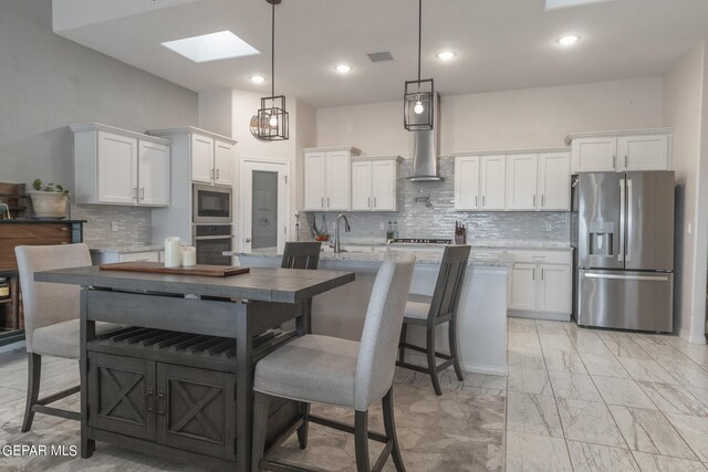 kitchen with a skylight, backsplash, stainless steel appliances, and hanging light fixtures