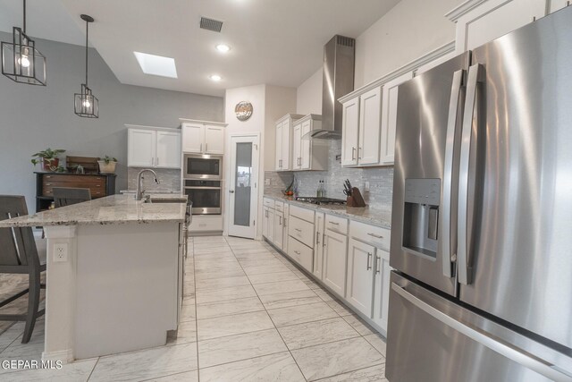 kitchen with a skylight, backsplash, white cabinets, stainless steel appliances, and an island with sink