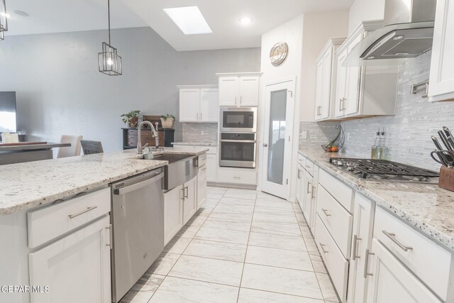 kitchen featuring wall chimney exhaust hood, appliances with stainless steel finishes, sink, white cabinetry, and a skylight