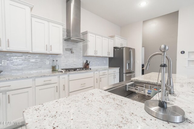 kitchen with white cabinets, appliances with stainless steel finishes, light stone countertops, and wall chimney exhaust hood