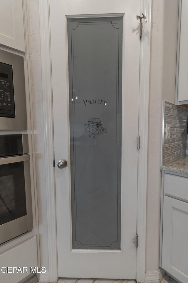 room details with white cabinets, light stone countertops, oven, and tasteful backsplash