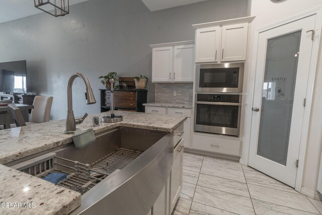 kitchen with light stone countertops, pendant lighting, appliances with stainless steel finishes, sink, and white cabinets