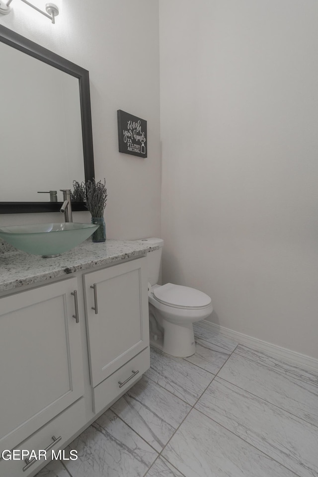 half bathroom with vanity, toilet, baseboards, and marble finish floor