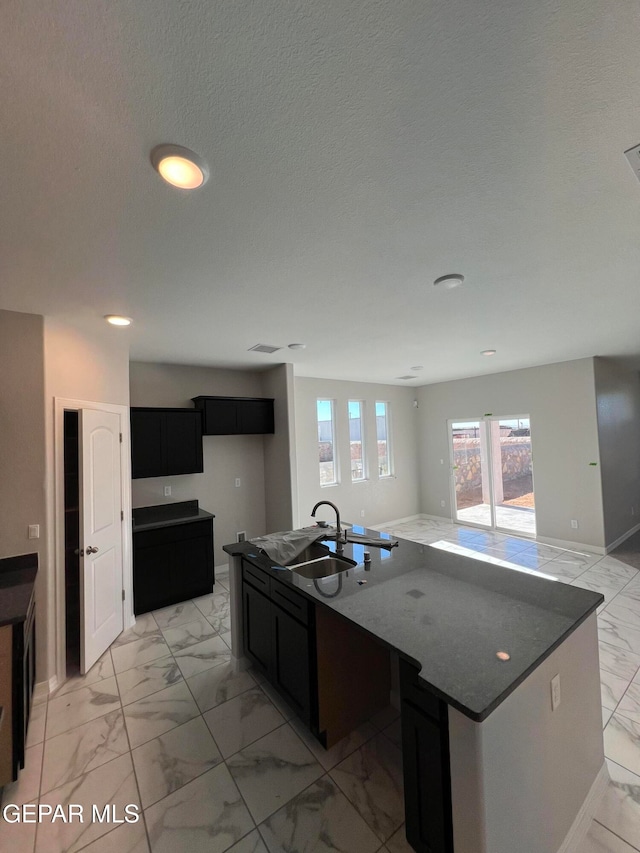 kitchen with sink, dark stone countertops, an island with sink, and a textured ceiling