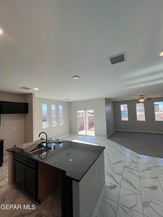 kitchen featuring a center island with sink, sink, ceiling fan, dark stone countertops, and a textured ceiling