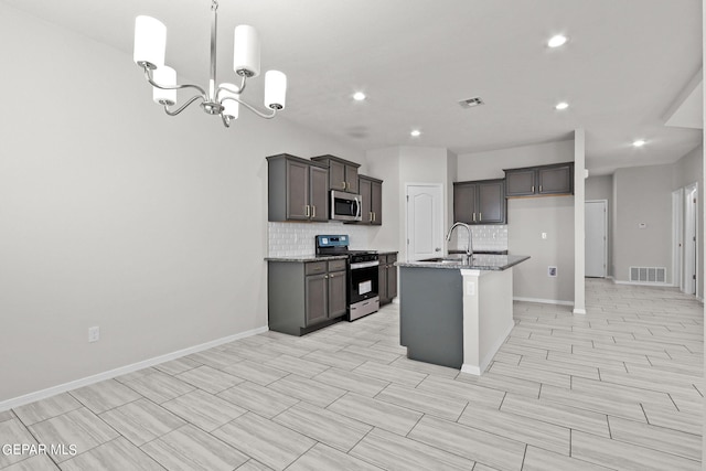 kitchen with an inviting chandelier, appliances with stainless steel finishes, a kitchen island with sink, sink, and light stone counters