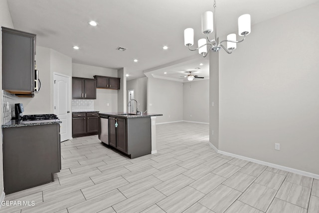 kitchen with appliances with stainless steel finishes, ceiling fan with notable chandelier, sink, an island with sink, and pendant lighting