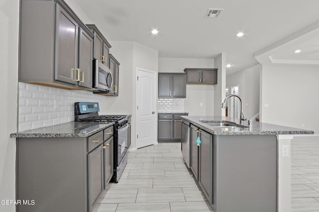 kitchen featuring dark stone countertops, stainless steel appliances, sink, gray cabinets, and a center island with sink