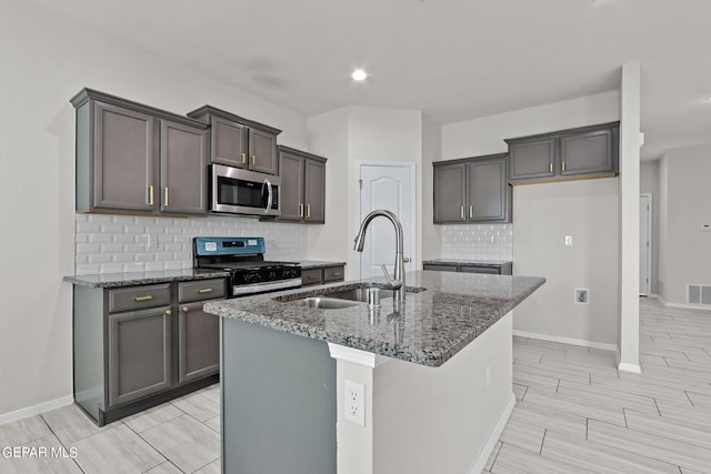 kitchen featuring dark stone counters, an island with sink, sink, decorative backsplash, and appliances with stainless steel finishes