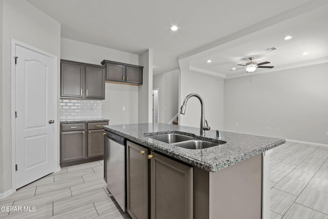 kitchen featuring dishwasher, an island with sink, light stone countertops, sink, and ceiling fan