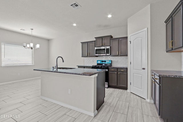 kitchen with a notable chandelier, an island with sink, sink, decorative backsplash, and appliances with stainless steel finishes