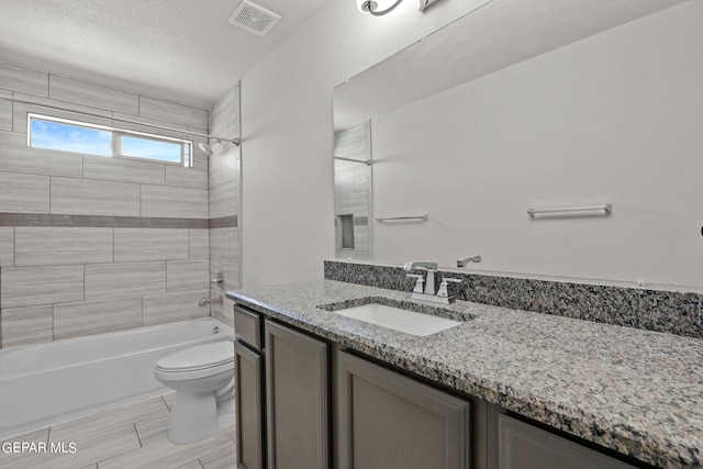 full bathroom featuring tiled shower / bath, vanity, toilet, and a textured ceiling