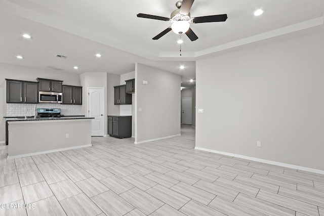 kitchen with light hardwood / wood-style flooring, ceiling fan, decorative backsplash, appliances with stainless steel finishes, and a center island with sink