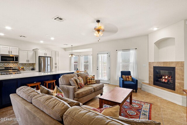 tiled living room featuring a fireplace, sink, and ceiling fan