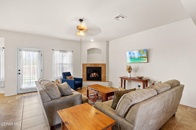 living room featuring ceiling fan, a tile fireplace, and light tile patterned flooring