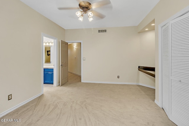 unfurnished bedroom with a closet, light colored carpet, ensuite bathroom, and ceiling fan