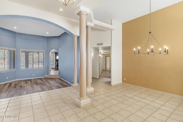 empty room with a notable chandelier, light wood-type flooring, decorative columns, and a high ceiling