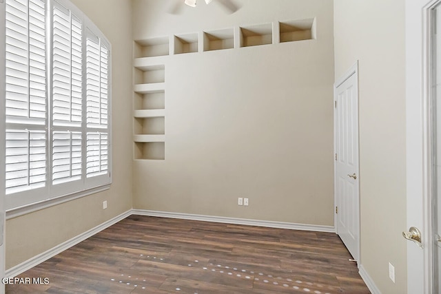 spare room featuring ceiling fan, a healthy amount of sunlight, built in shelves, and dark wood-type flooring