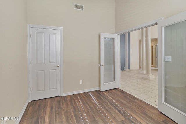 unfurnished bedroom with ornate columns, hardwood / wood-style flooring, and a high ceiling