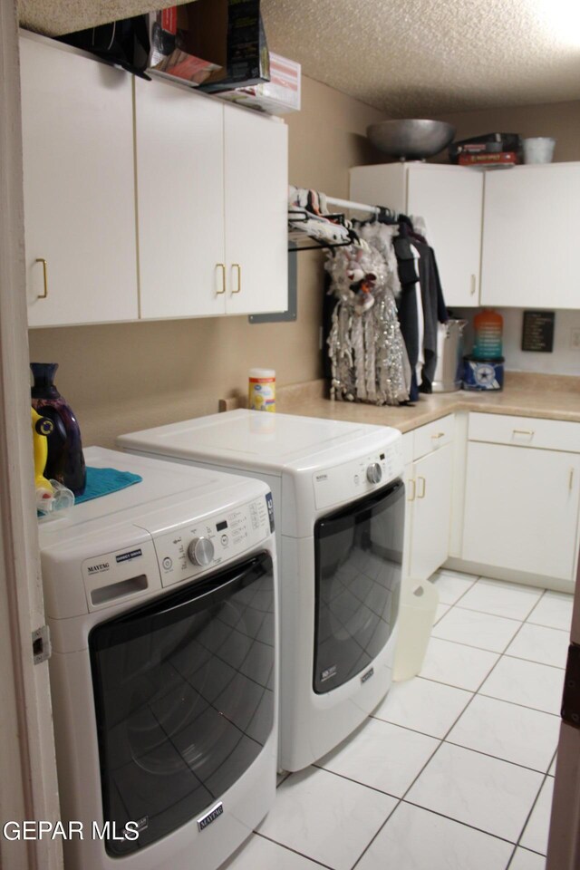 laundry room with cabinets, light tile patterned flooring, washer and dryer, and a textured ceiling