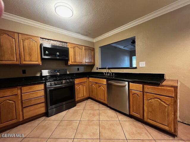 kitchen with light tile patterned flooring, appliances with stainless steel finishes, sink, ornamental molding, and a textured ceiling