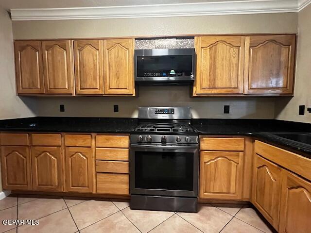 kitchen with ornamental molding, stainless steel appliances, dark stone counters, and light tile patterned floors