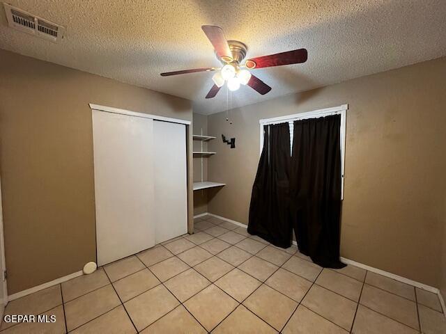 unfurnished bedroom with ceiling fan, a textured ceiling, a closet, and light tile patterned floors