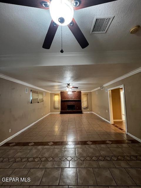 unfurnished living room with crown molding, ceiling fan, a textured ceiling, a brick fireplace, and tile patterned floors