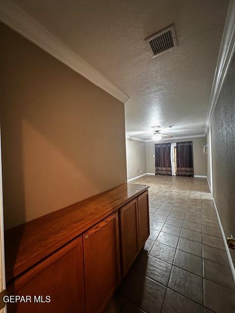 hallway featuring ornamental molding, light tile patterned flooring, and a textured ceiling